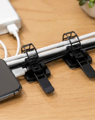 Pack of 25 Problems Solved 3M self-adhesive cable organizers for desks, showing black cable clips attached to a desk surface.